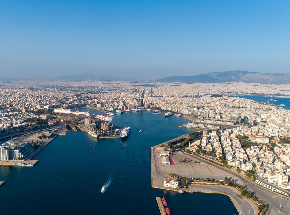 Drone flight over Piraeus harbor showing ships docked plus and Athens and mountains in the distance